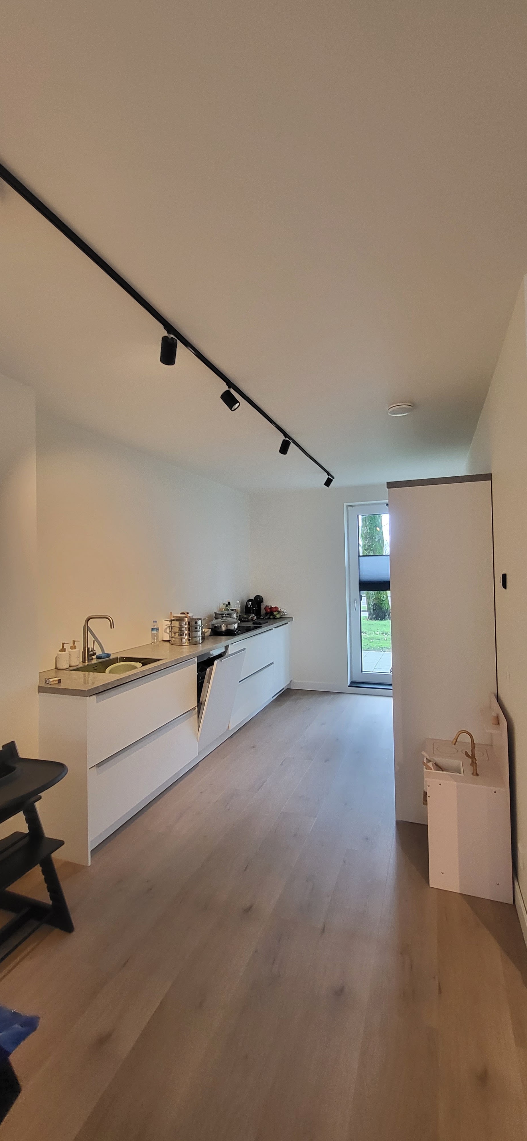 Lichte woonruimte met witte keuken, houten vloer en railverlichting