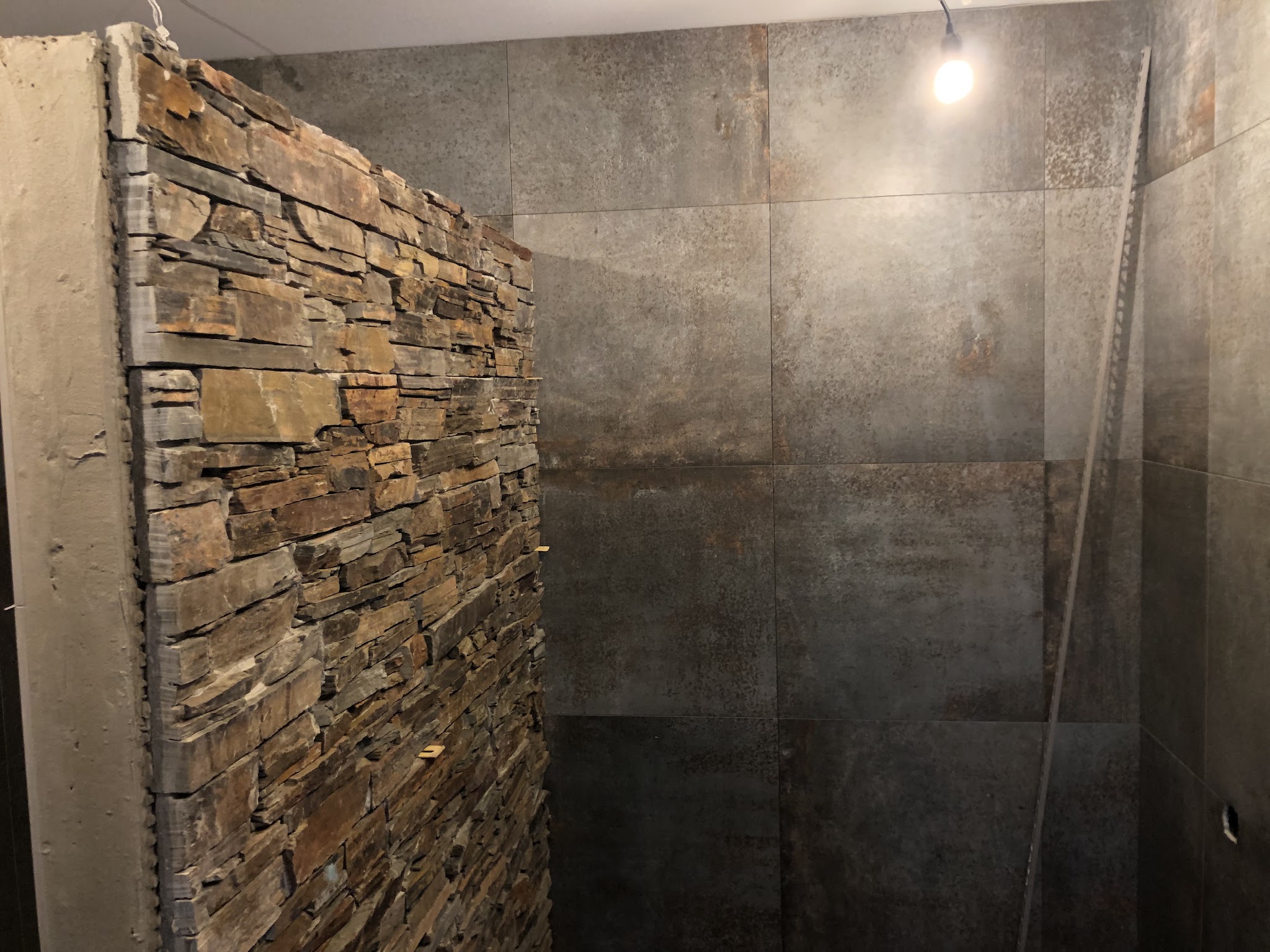 Douche met wand van natuurstenen strips en grote donkere tegels